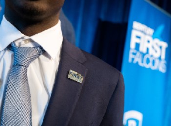 Close-up photo of Black male student wearing a blue suit and tie, with a Bentley First Gen pin in his lapel