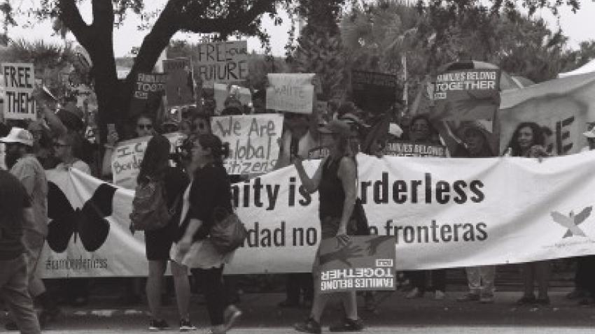 Black and white photo of protestors holding signs that say "We are global citizens" and "Humanity is borderless."