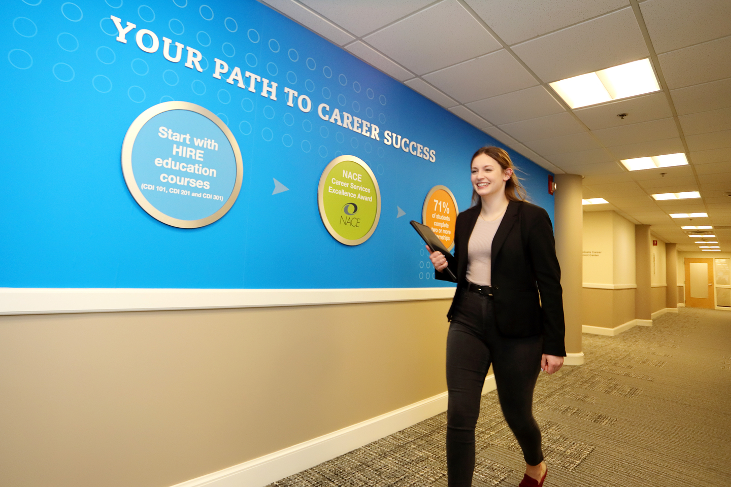 Female student walking down a hallway with signage from the Pulsifer Career Development Center on the wall. 