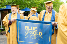 Blue and Gold Society members get ready to march at Commencement holding a banner of that reads, "Blue & Gold Society"