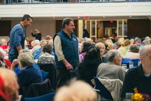 Man smiling amid crowd of people seated for luncheon