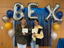 Two people smiling in front of BEX balloons