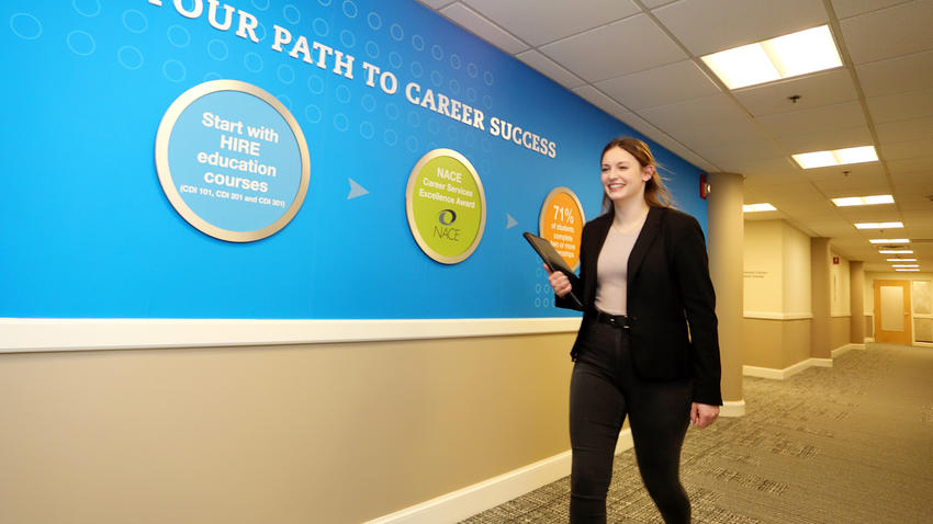 Female student walking down a hallway with signage from the Pulsifer Career Development Center on the wall. 