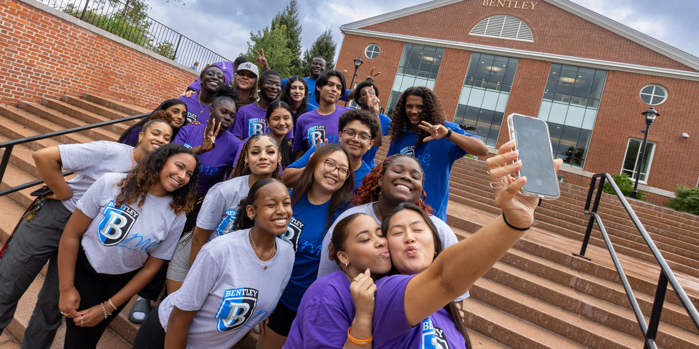 smiling students stand on steps outside Bentley Library and take a photo of themselves 