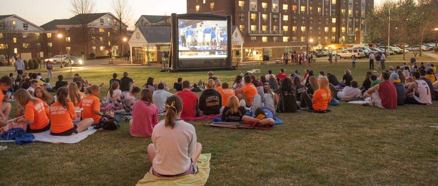 students watching a film on a large outdoor screen