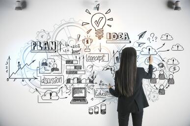 Woman in black pant suit writing business ideas on a white wall