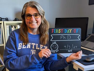 Kathi Kaiser holds a sign commemorating her first day of the Bentley Executive PhD in Business program